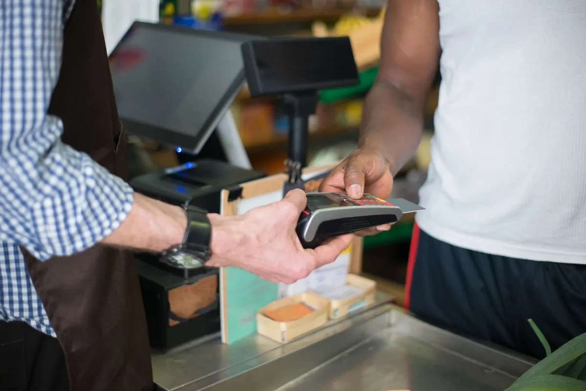 A customer inserts a card into a card reader held by a cashier at a store checkout counter